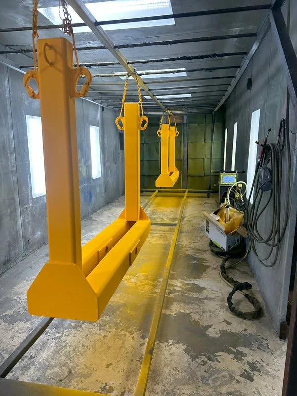 Yellow industrial lifting hooks suspended from a rail system inside a workshop or warehouse.
