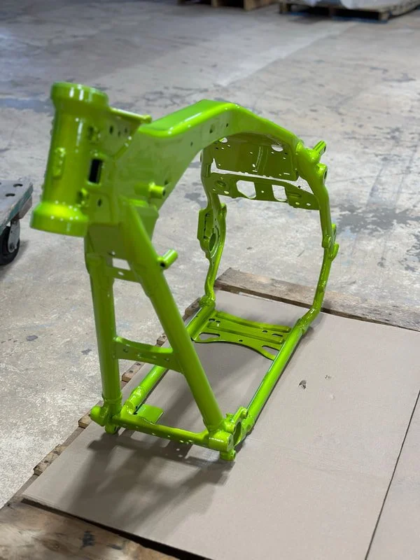Green metal frame of a small aircraft or drone on a concrete floor.