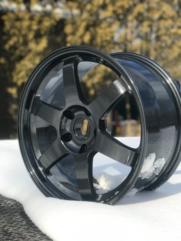 A black plastic wheel rim resting on snow with a blurred outdoor background.