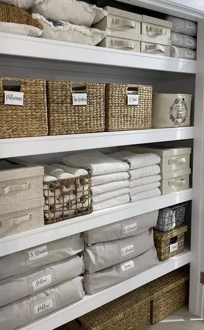 Organized shelves with baskets, folded towels, and storage boxes in a closet or linen closet.