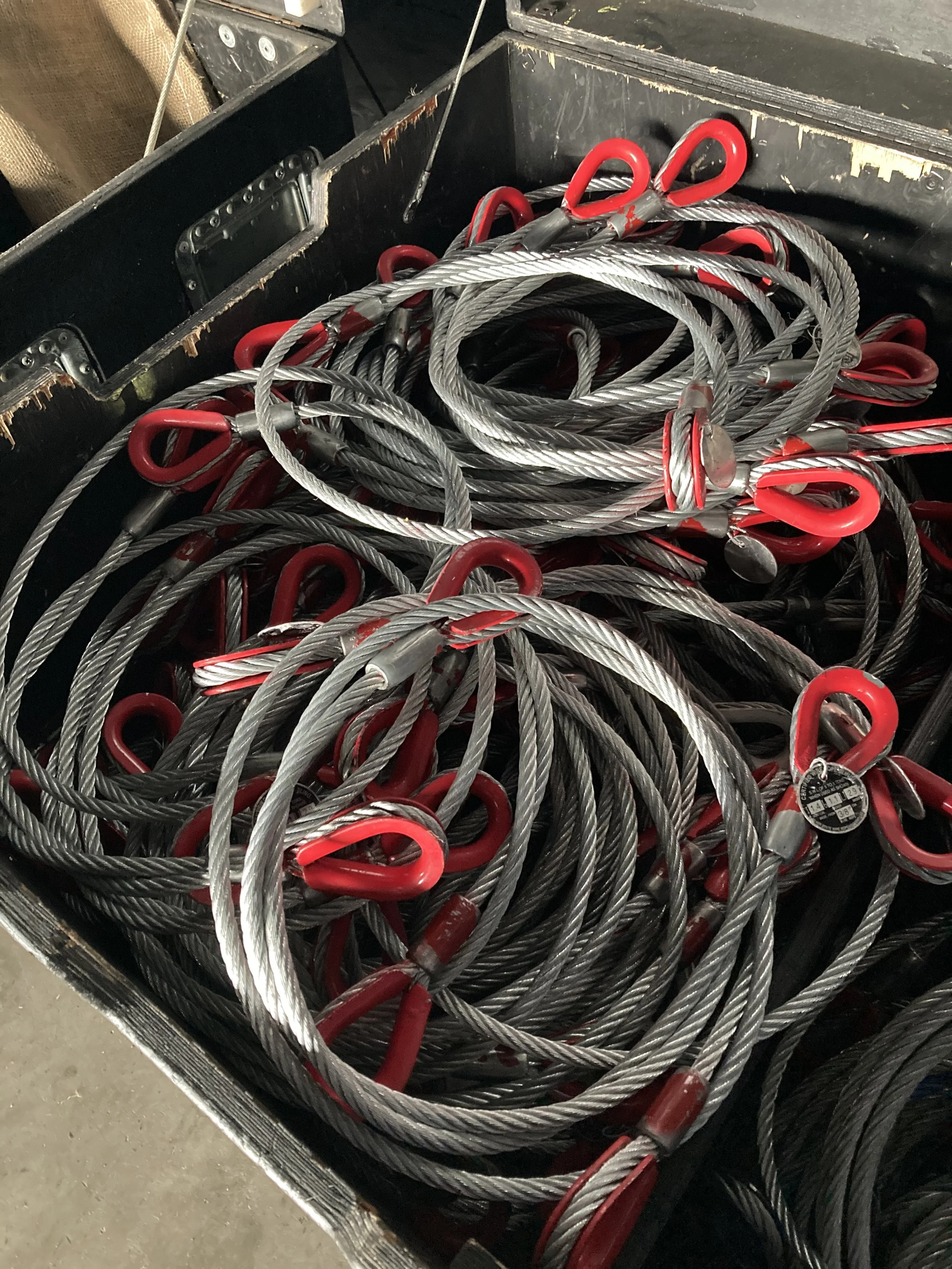 A black storage box filled with coiled steel cables with red hooks at the ends.