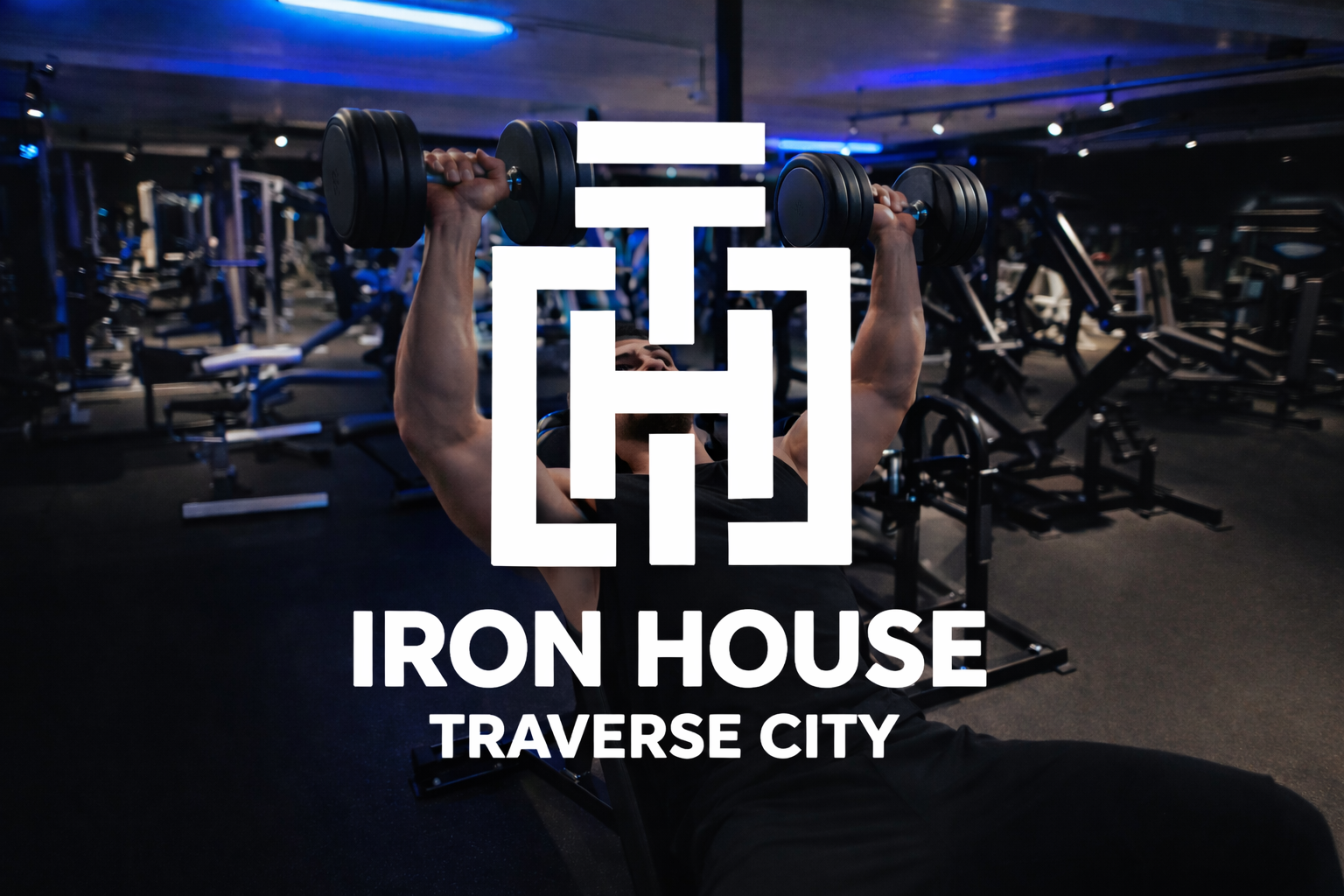 A man lifting dumbbells in a gym with black and blue lighting, surrounded by workout equipment. The overlay text reads "Iron House Traverse City."