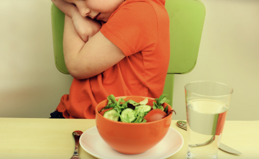 Niño sentado a la mesa rechazando un plato de ensalada, imagen que representa dificultad para aceptar límites y tolerar la frustración.