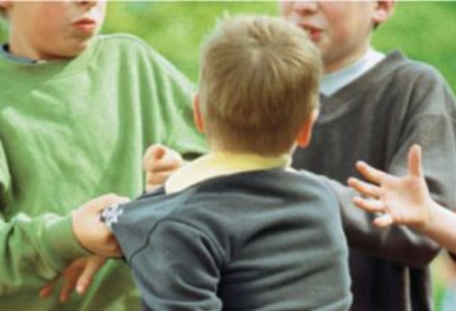 Tres niños discutiendo al aire libre, uno con camiseta verde, otro con sudadera gris y otro con camisa y suéter oscuro.