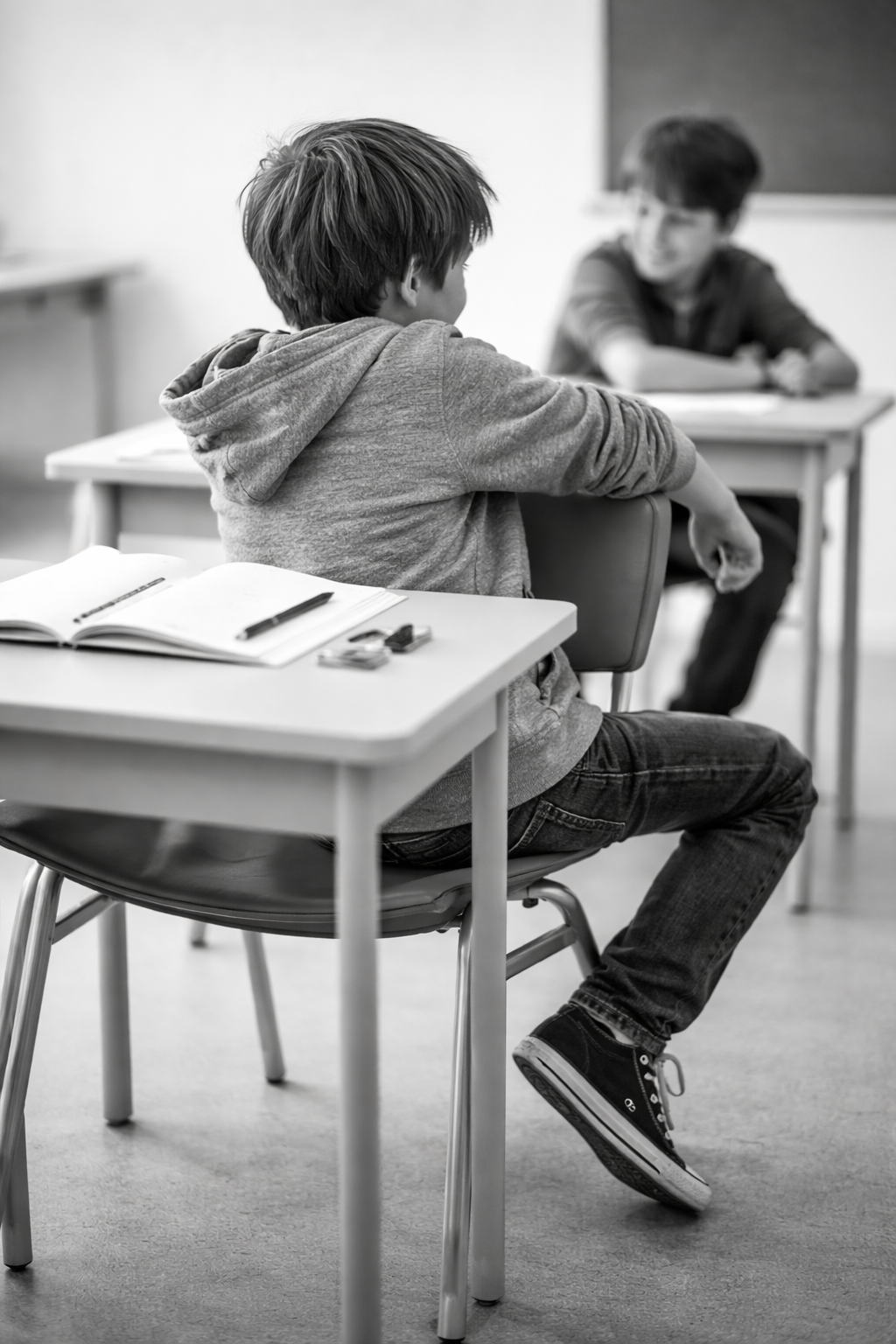 Niño de espaldas en un aula, girado hacia un compañero, con cuaderno y lápiz sobre el pupitre, imagen asociada al TDAH de presentación combinada.