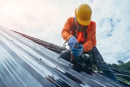 Worker in safety gear installing solar panels on a roof.