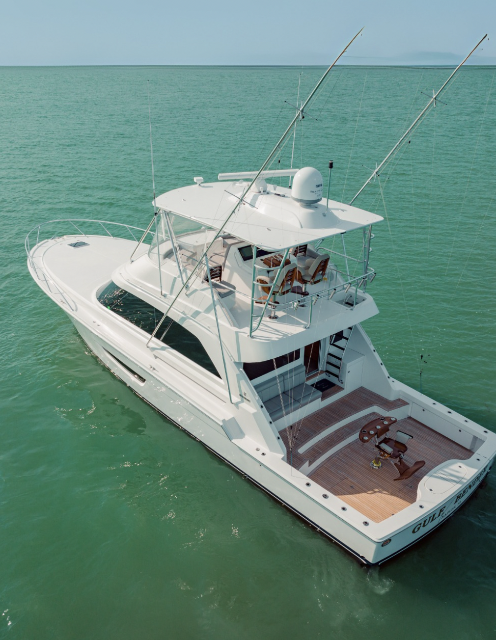 A white yacht floating on calm green water with clear sky in the background.