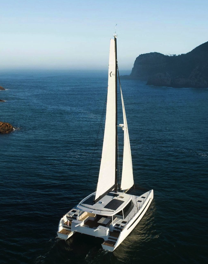 A large white sailboat on the ocean near rocky cliffs.