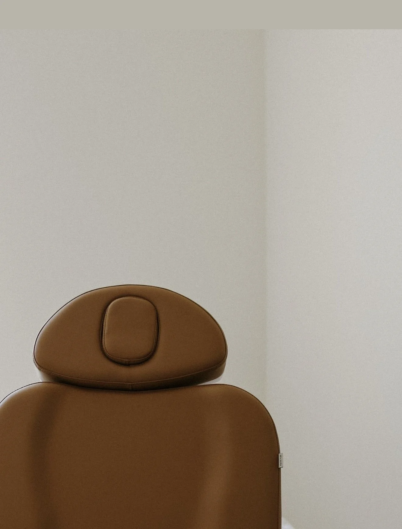 Close-up of a brown medical examination chair with a headrest against a plain white wall.