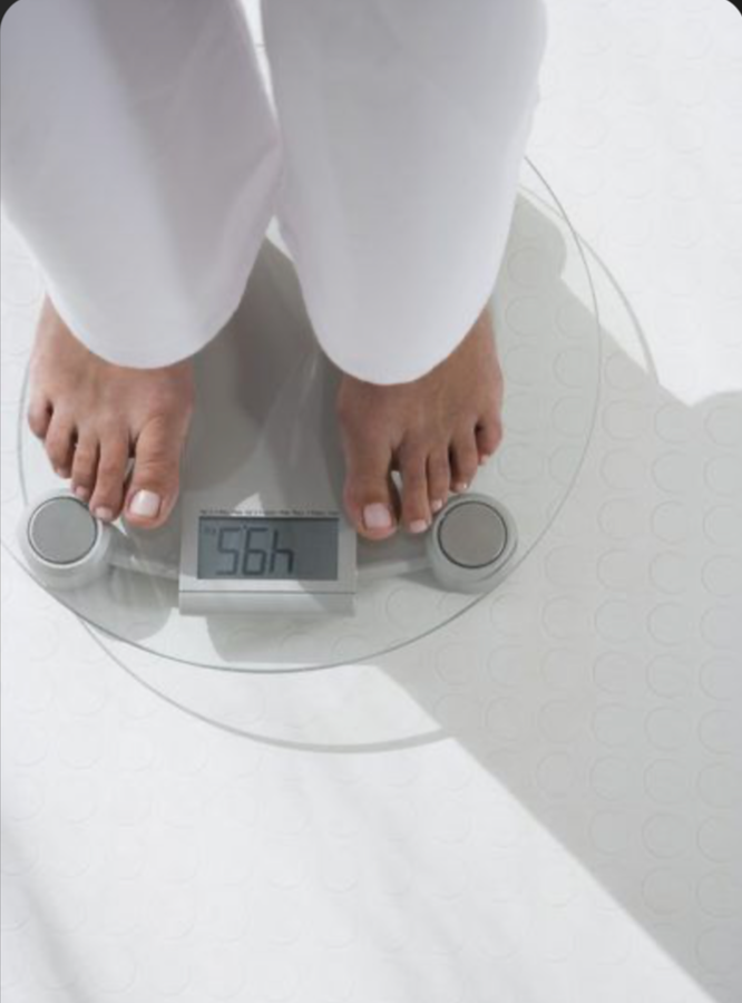 A person standing on a digital scale inside a medical facility, showing a weight of 150.6 pounds.