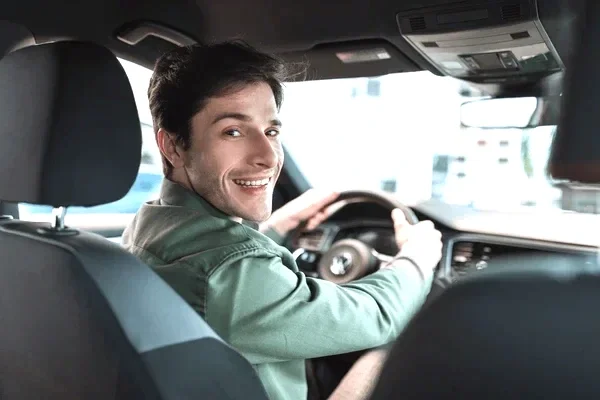 A smiling man driving a car, looking back over his shoulder.