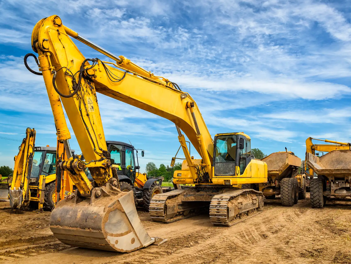 Yellow excavators and construction vehicles parked on dirt under a partly cloudy sky.