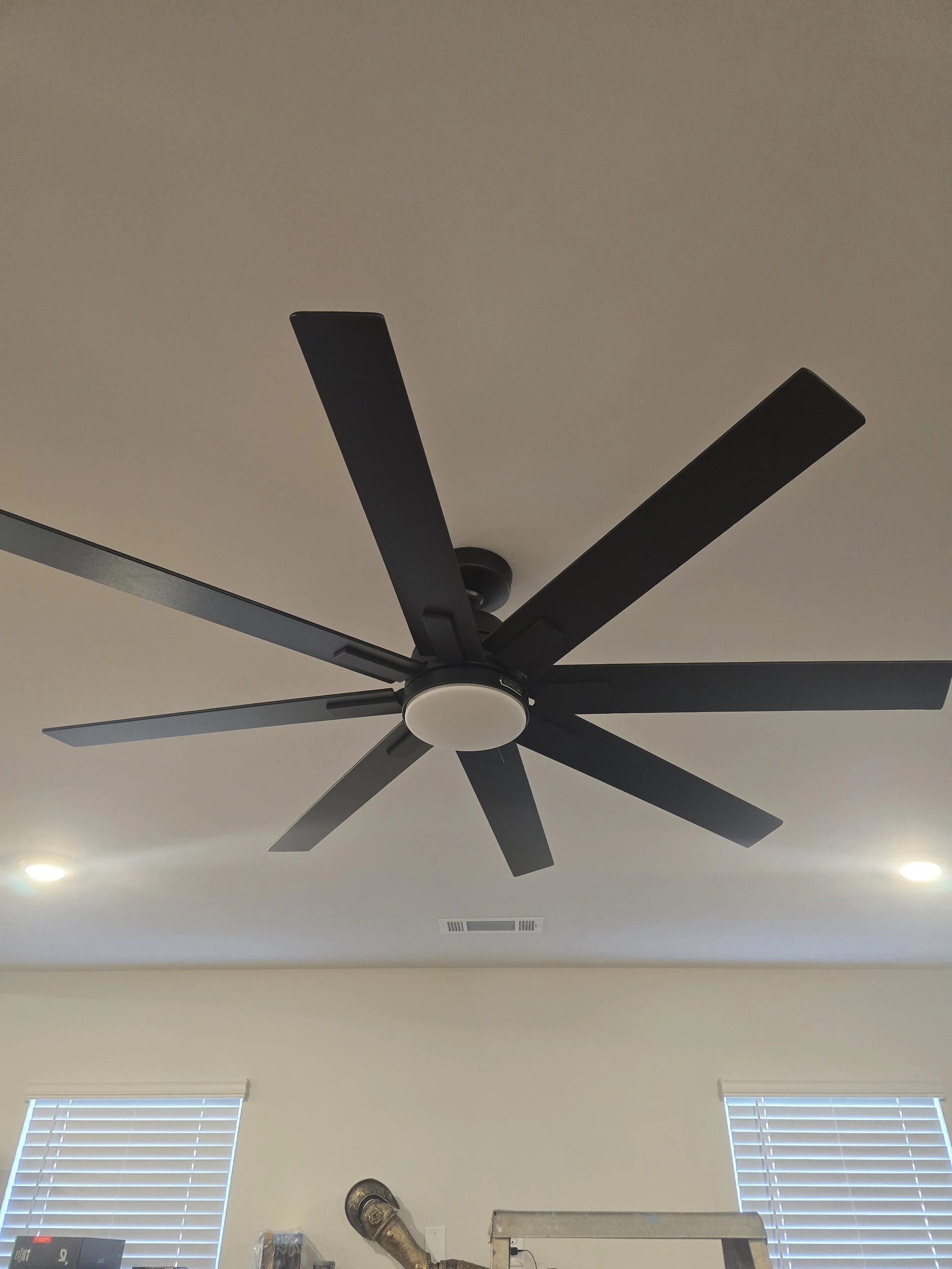 Ceiling fan with black blades and a white light fixture in a room with two windows and ceiling vents.