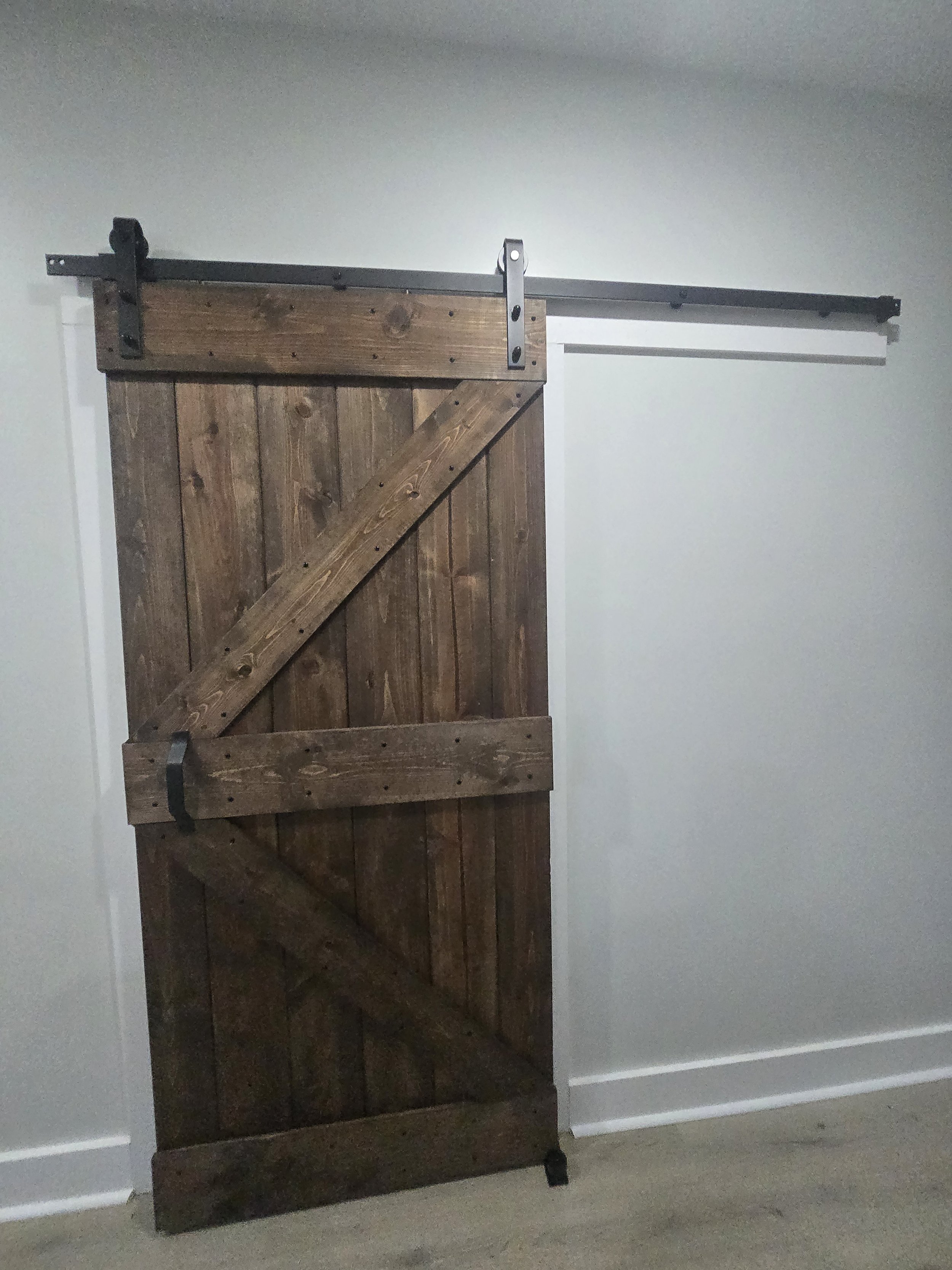 A wooden sliding barn door mounted on a black metal track in a room with white walls.