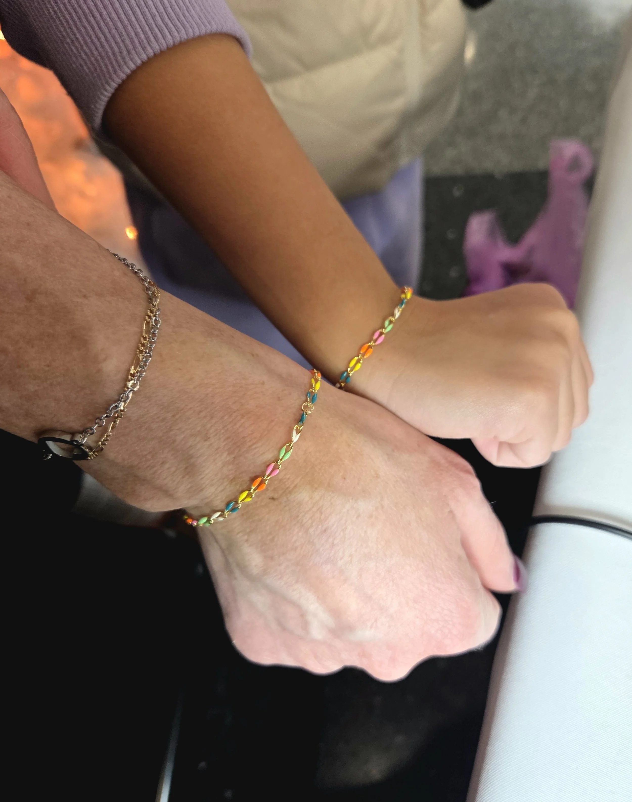 Two people holding hands, one wearing a rainbow-colored bracelet and the other wearing a silver bracelet.