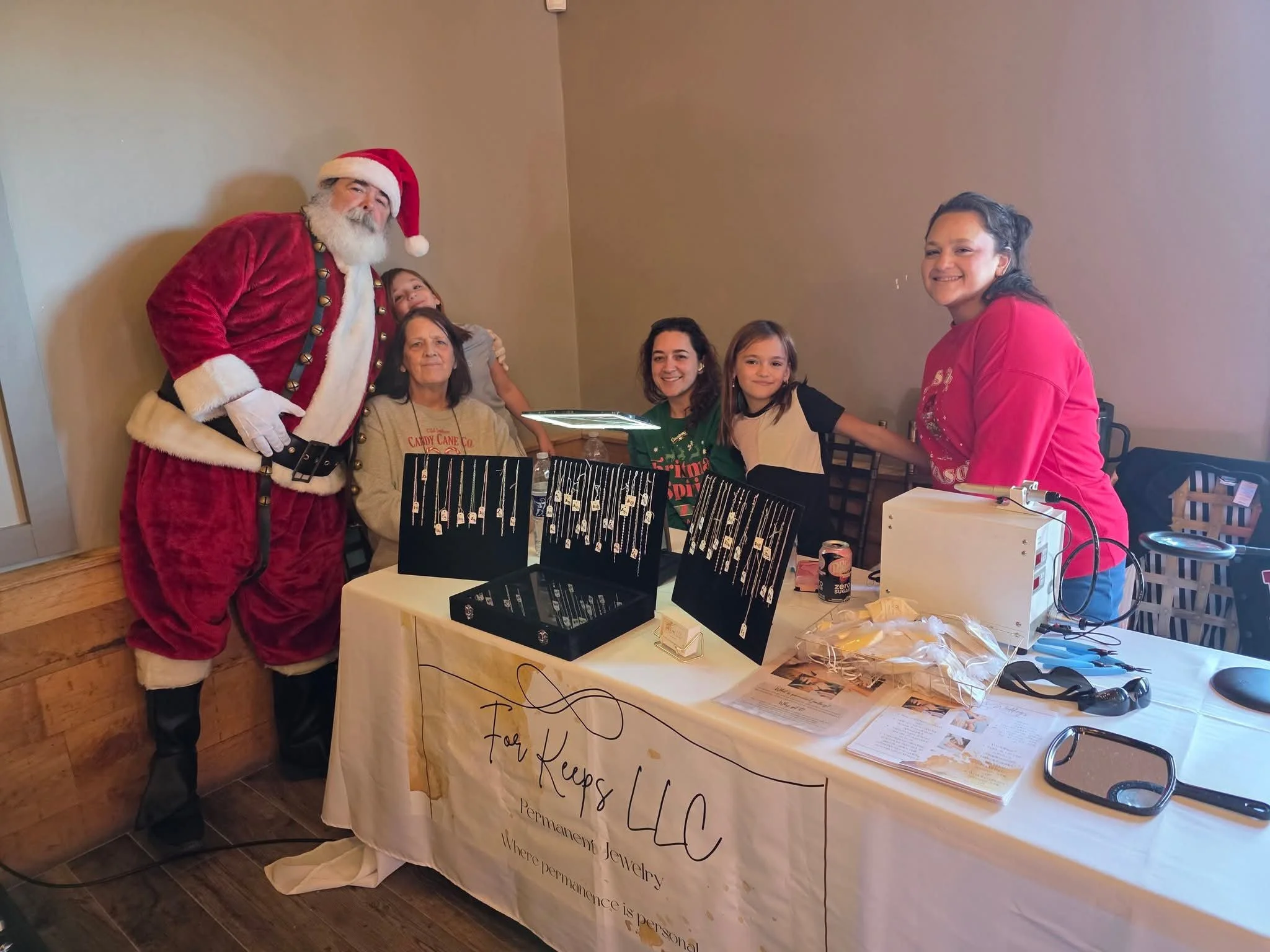 Santa Claus standing with four women and one girl behind a jewelry display table during a holiday event.