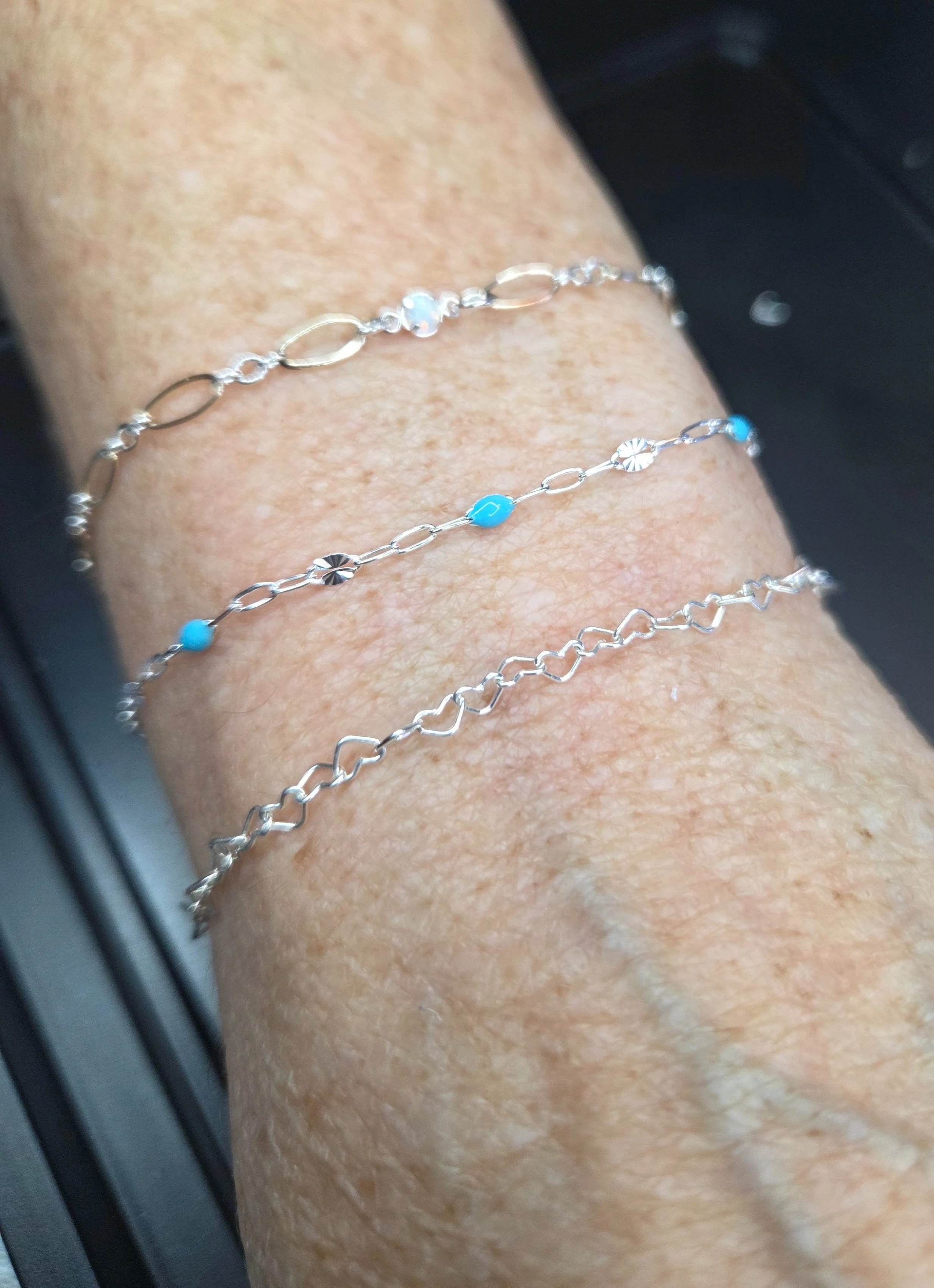 Three silver bracelets with turquoise and decorative charms worn on a person's wrist.