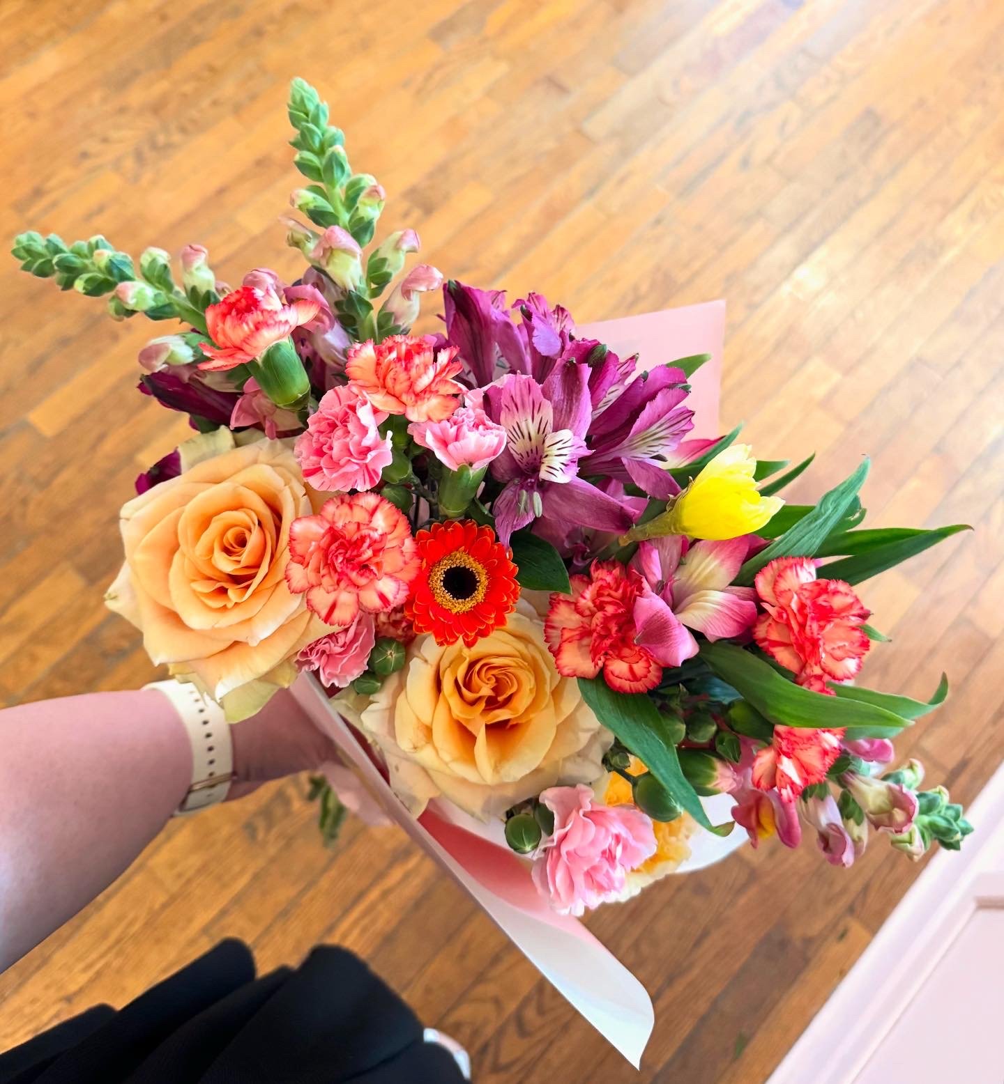 Bouquet of colorful flowers including roses, carnations, alstroemeria, and snapdragons, wrapped in pink paper.