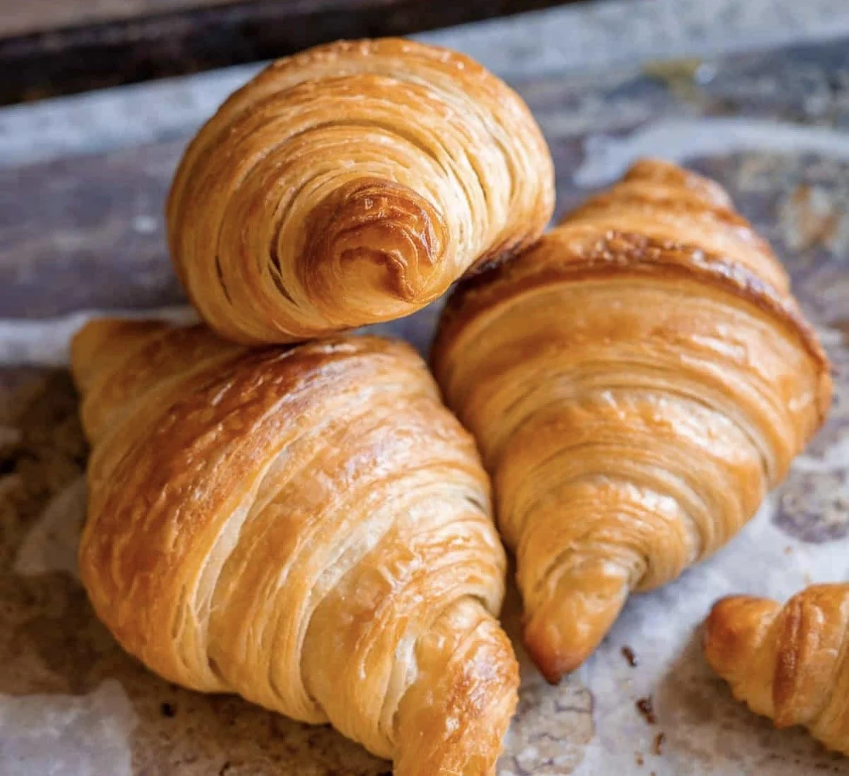 Three golden-brown croissants on a wooden surface.