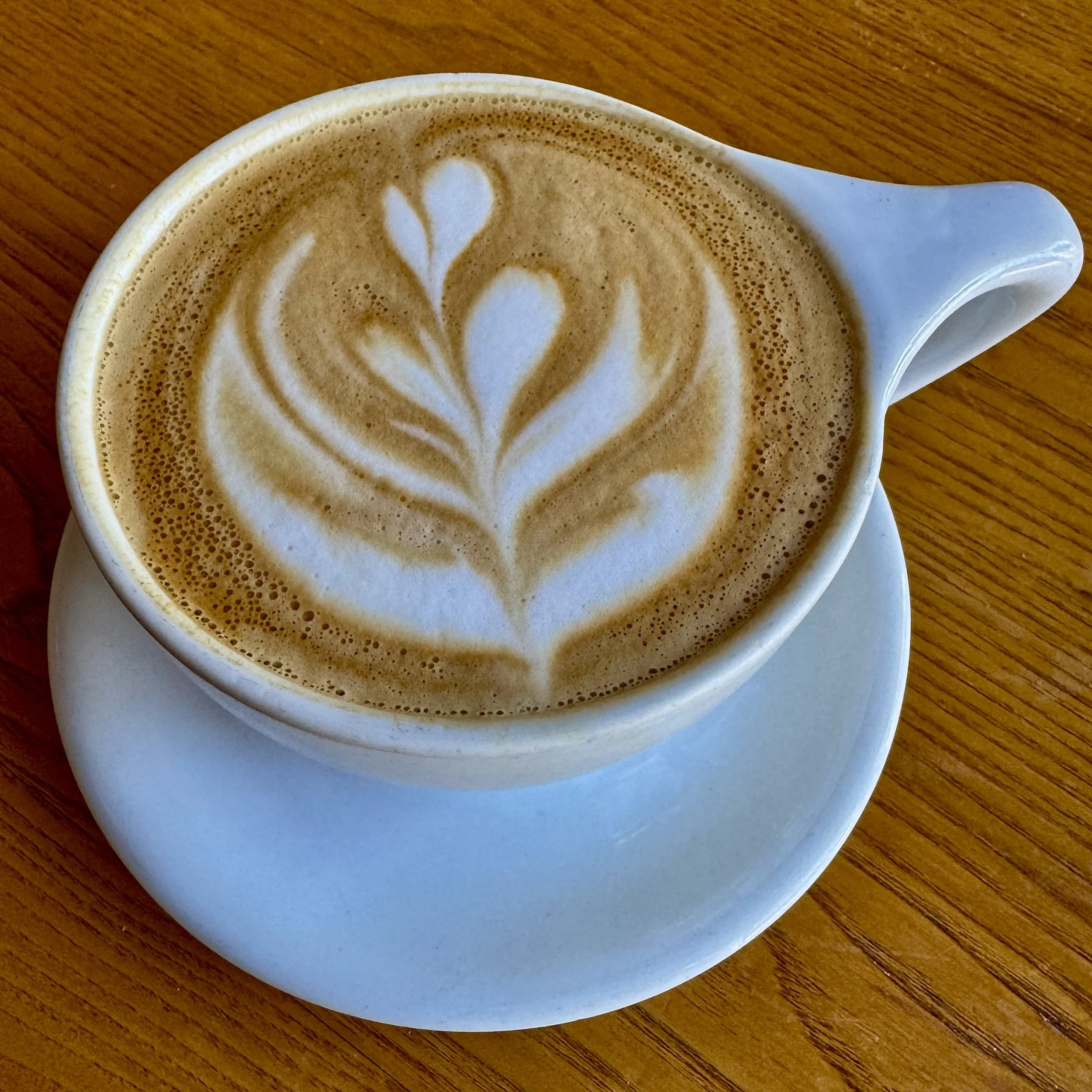 A cup of cappuccino with latte art in a white cup on a matching saucer on a wooden table.