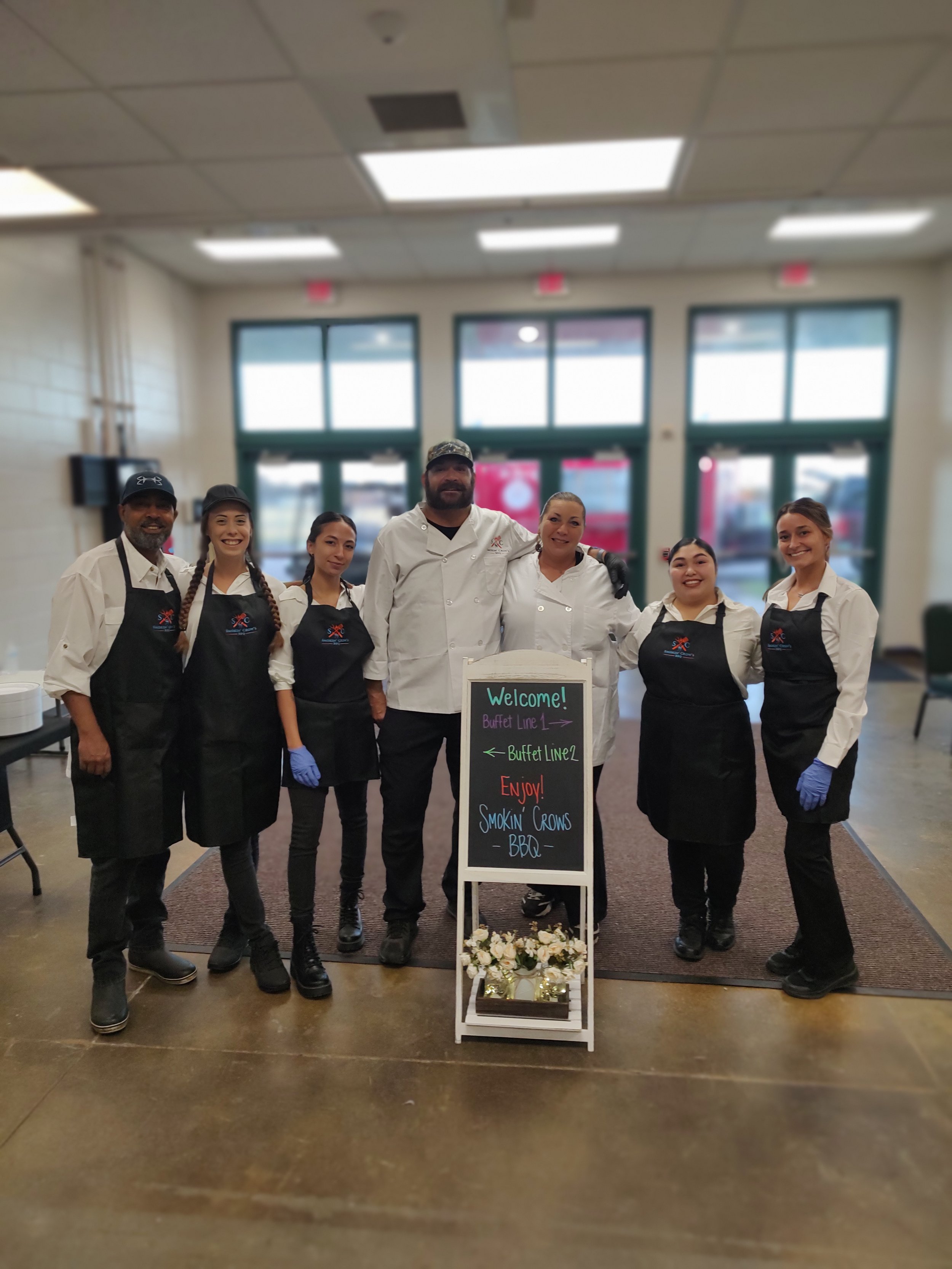 Smokin’ Crow’s BBQ catering team standing together at an event venue, welcoming guests at a professionally staffed buffet service.