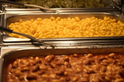 Chafing pans filled with classic barbecue sides including mac and cheese and baked beans prepared for catered events.