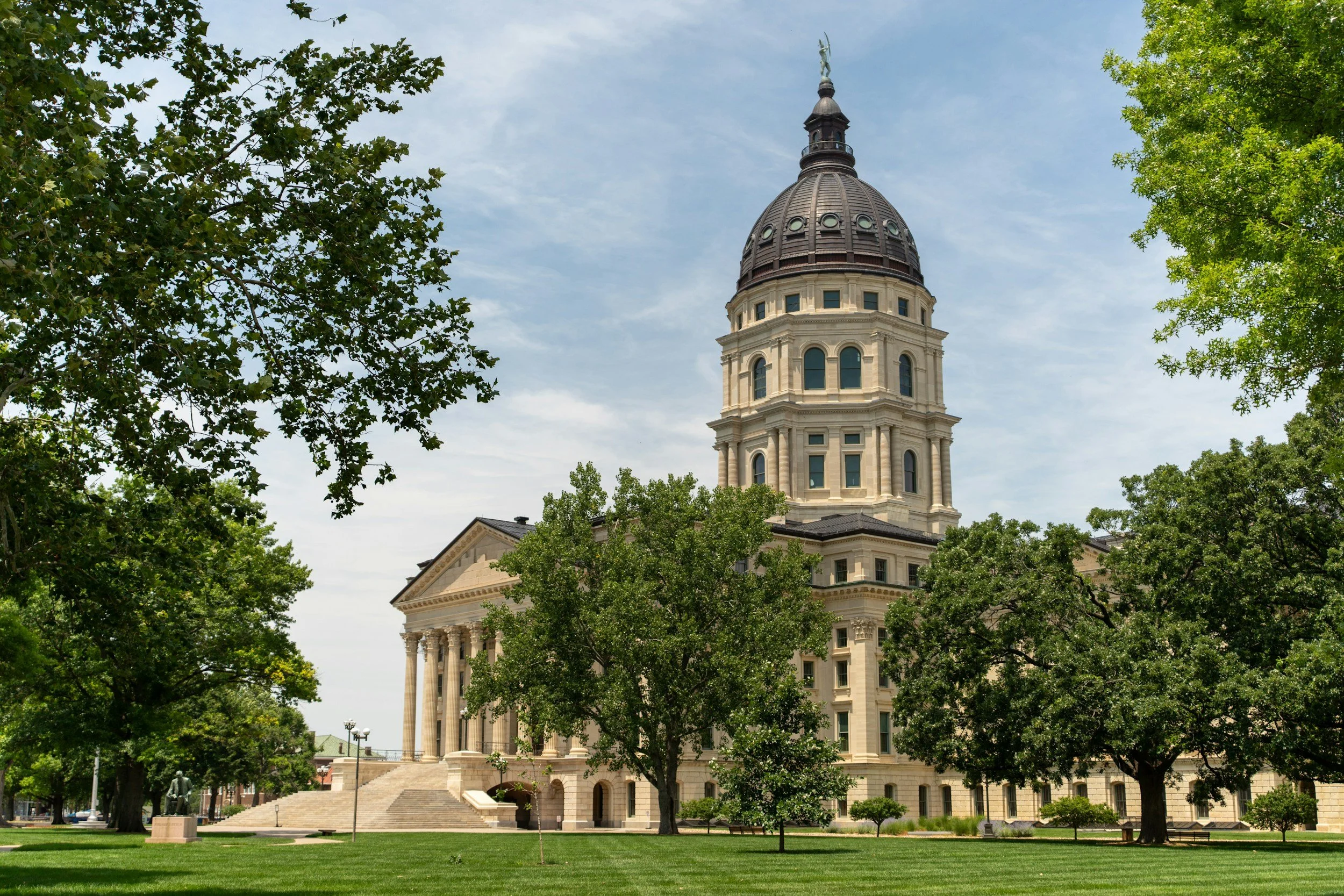 The Texas State Capitol building seen through green trees on a sunny day, with a clear blue sky overhead.