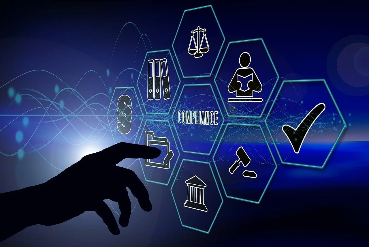 Digital illustration of compliance concepts, including legal scales, files, a person reading, a checkmark, a gavel, and government building icons, with a hand interacting with the icons.