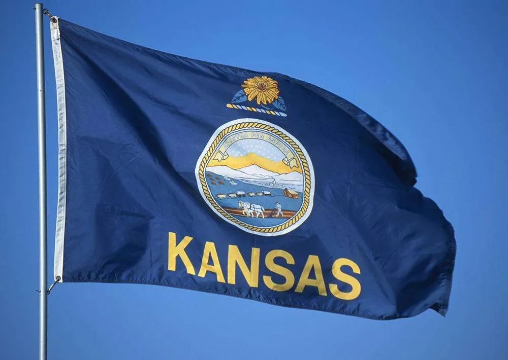 Kansas state flag waving in the wind against a blue sky.