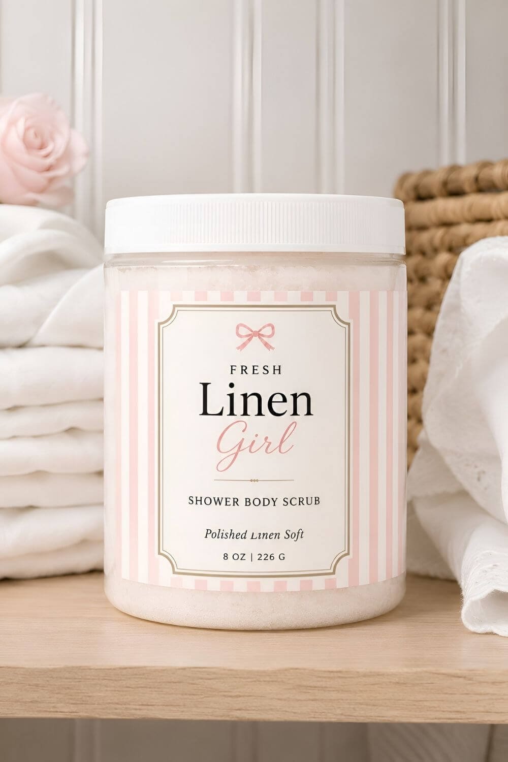 Fresh Linen Girl Shower Body Scrub in an 8 oz clear jar with a pink-and-cream striped label, white sugar scrub, white lid, folded towels, and a soft clean bathroom shelf background.