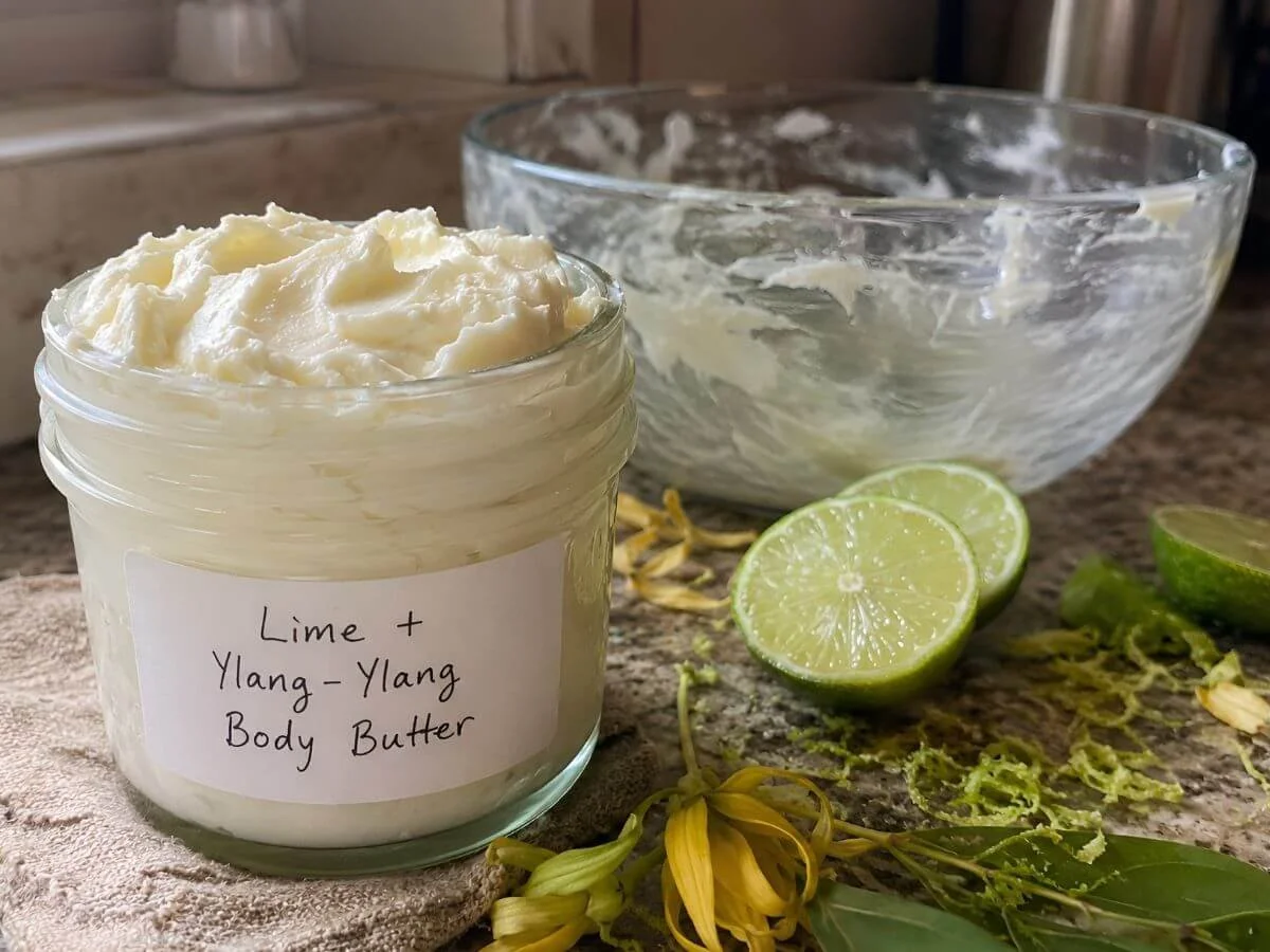Homemade lime ylang-ylang body butter in a labeled glass jar with fresh limes.