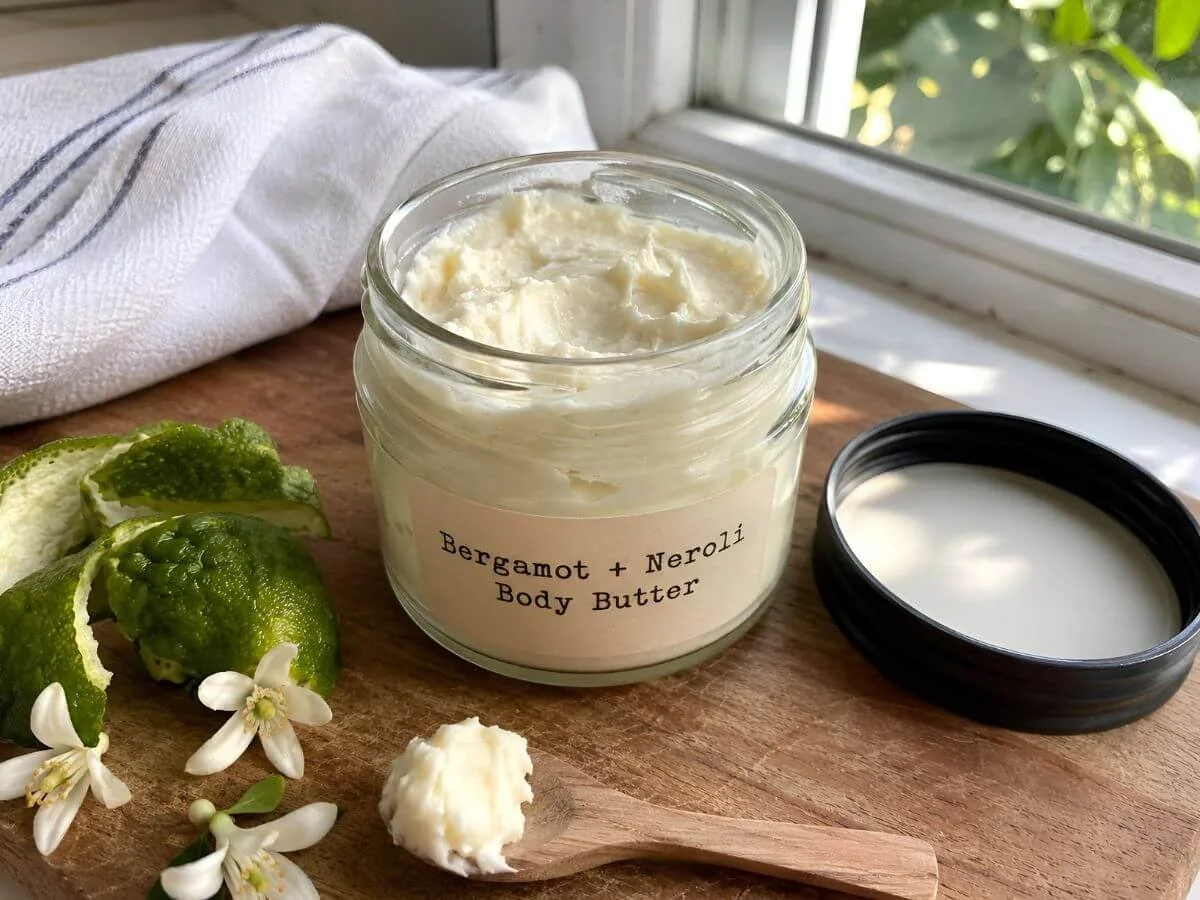 Homemade bergamot neroli body butter in a glass jar with citrus peel and white blossoms.