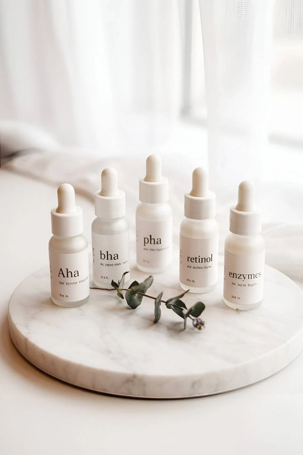 A clean, labeled flat lay featuring small glass bottles or droppers labeled “AHA,” “BHA,” “PHA,” “Retinol,” and “Enzymes.” White or marble background, soft focus, modern typography.