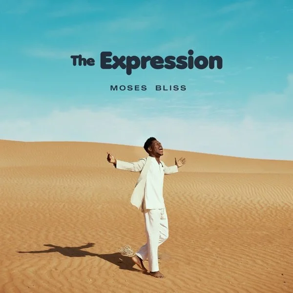 A man standing barefoot in a vast desert, appearing joyful with arms outstretched. The sky is bright blue with some clouds. Text on the image reads "The Expression" by Moses Bliss.