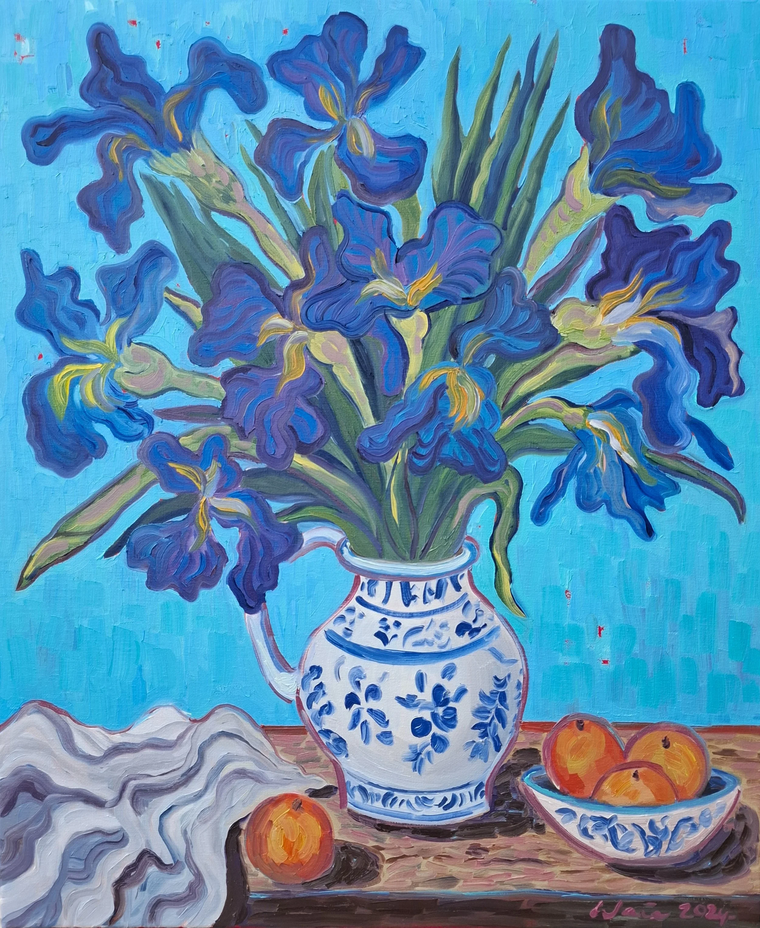 A vibrant still life painting of blue irises in a white porcelain vase with blue floral patterns, set on a rustic wooden table. There is a bowl with oranges and a white cloth on the table. The background is a solid light blue color.