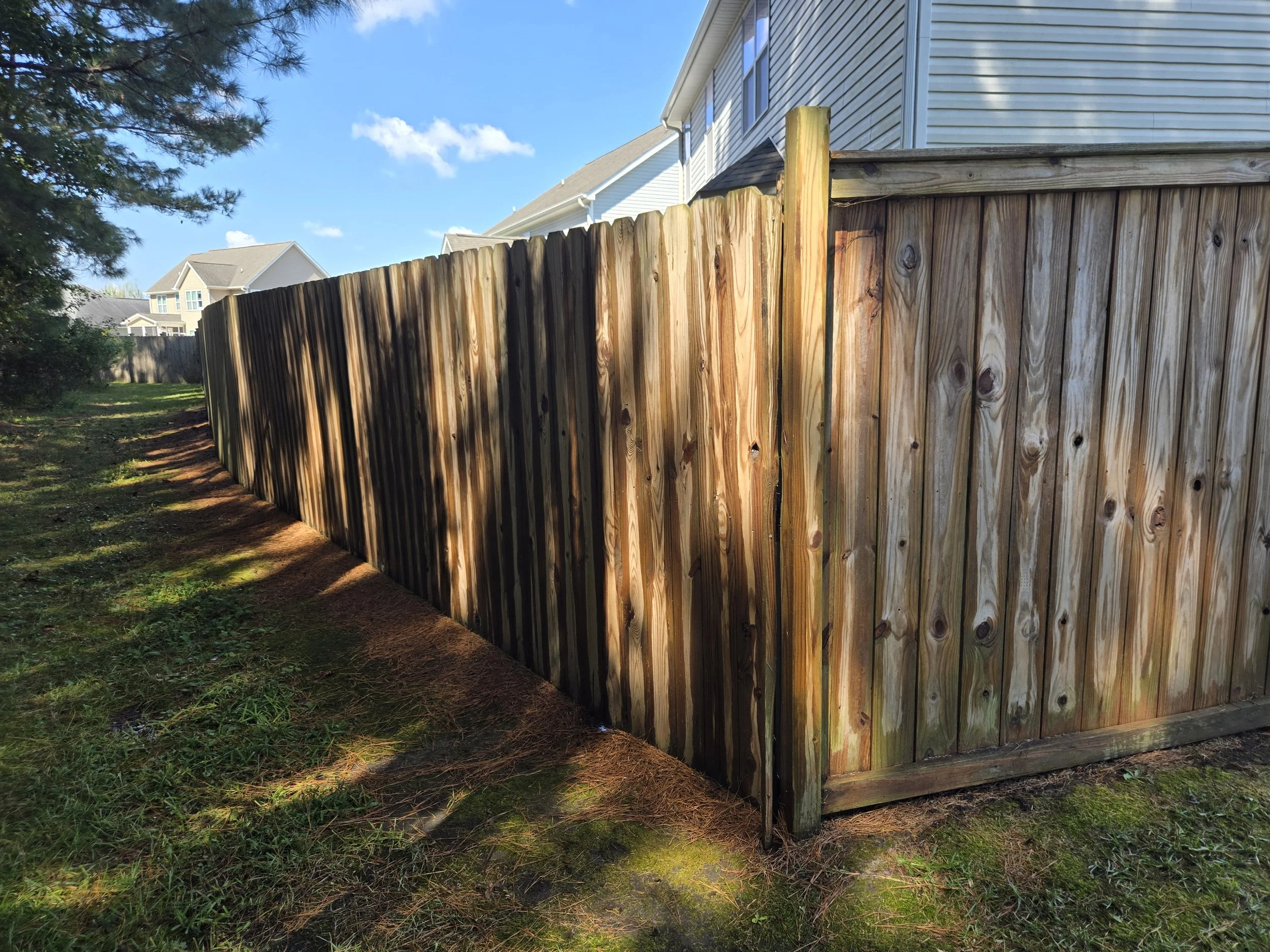 A freshly cleaned, wooden privacy fence runs along the side of a residential yard.