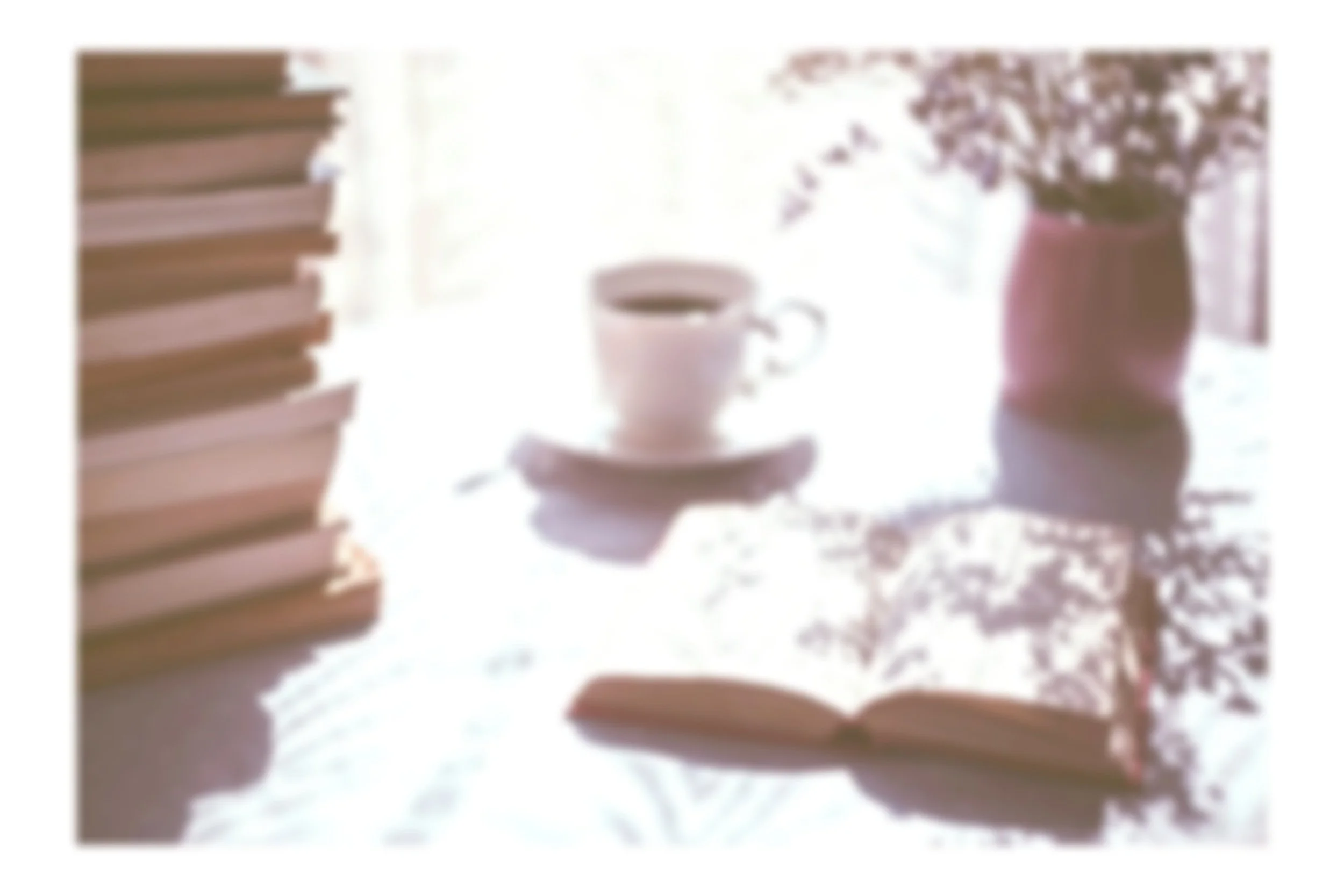a stack of books on the left, a white cup filled with coffee in the center, an open book in the foreground.