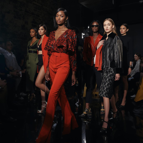 Group of diverse female models walking on runway during a fashion show, wearing stylish and colorful outfits.