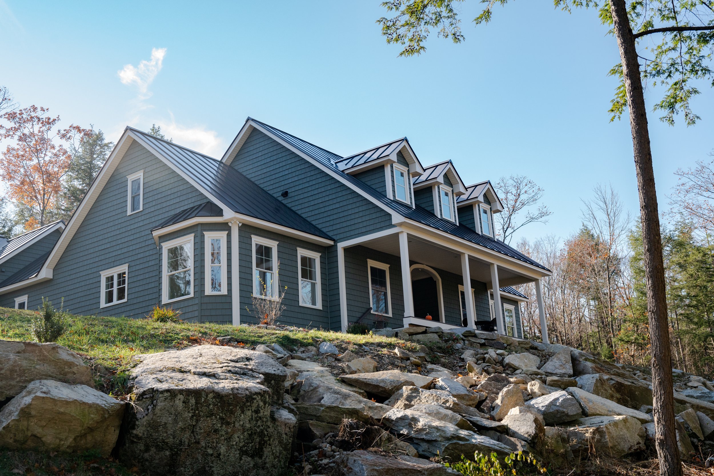 Side view of the Country Cape with a bay window, standing seam metal roof, and natural stone slope