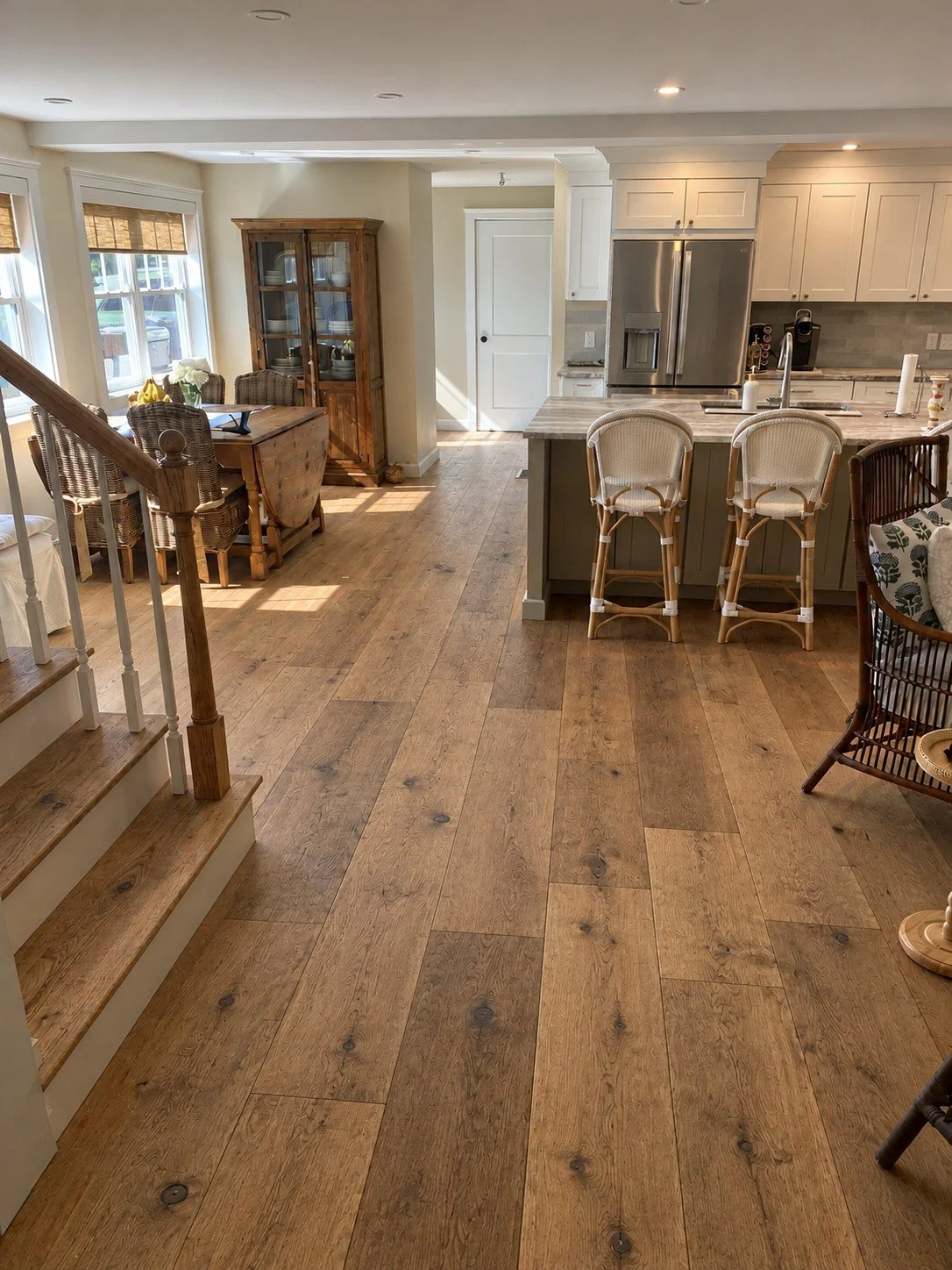 Open living and kitchen area with wide-plank oak floors, a wood stair, a dining table, and an island with bar stools
