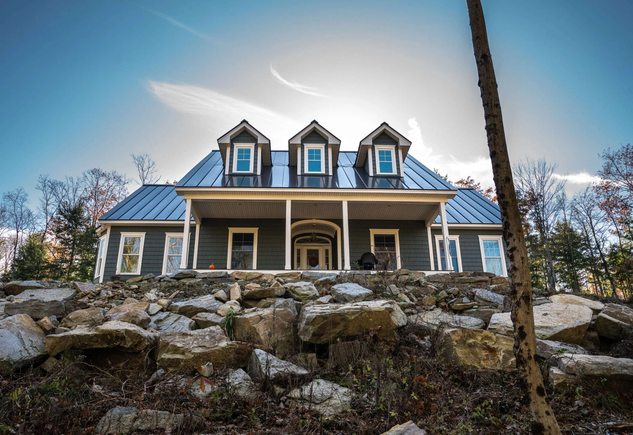 Front of a four-bedroom Country Cape with three dormers and a covered porch on a wooded New Hampshire hillside