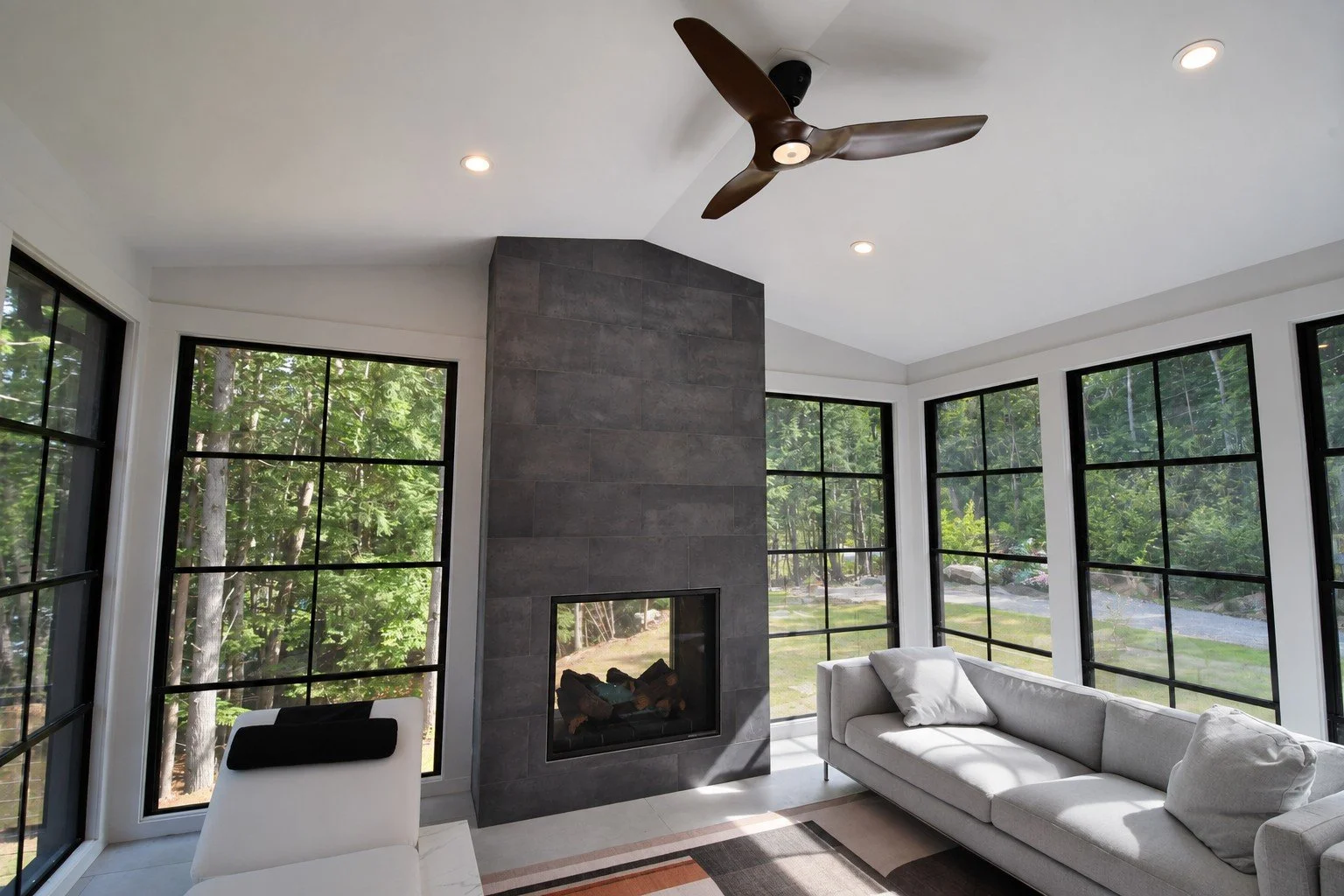 Sunroom with a ceiling fan, a gray stone fireplace, a white sofa, and black-framed windows