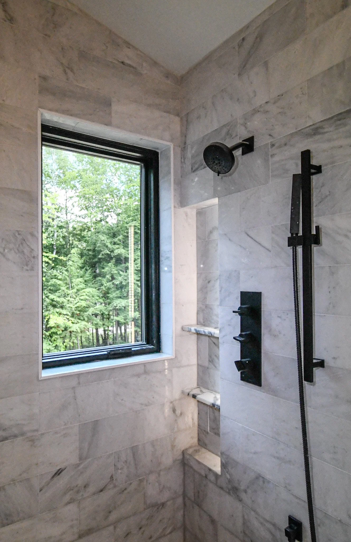 Tiled walk-in shower with black fixtures and a window