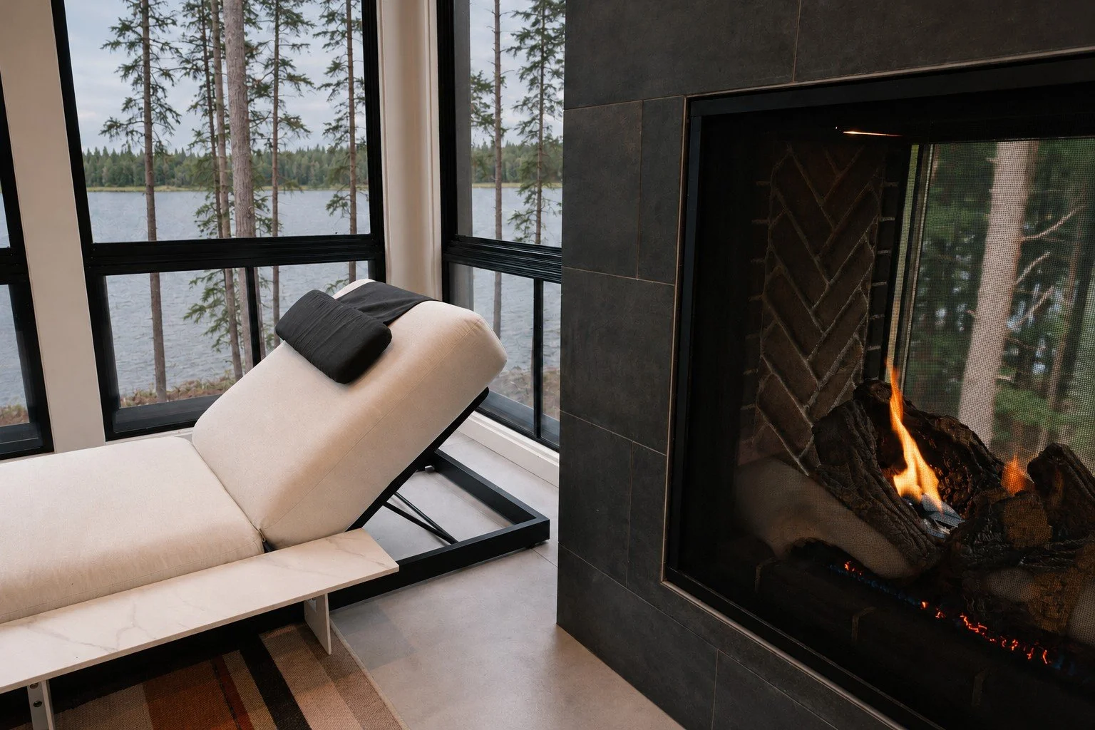 Lounge chair beside a see-through gas fireplace with a view of the lake through the windows