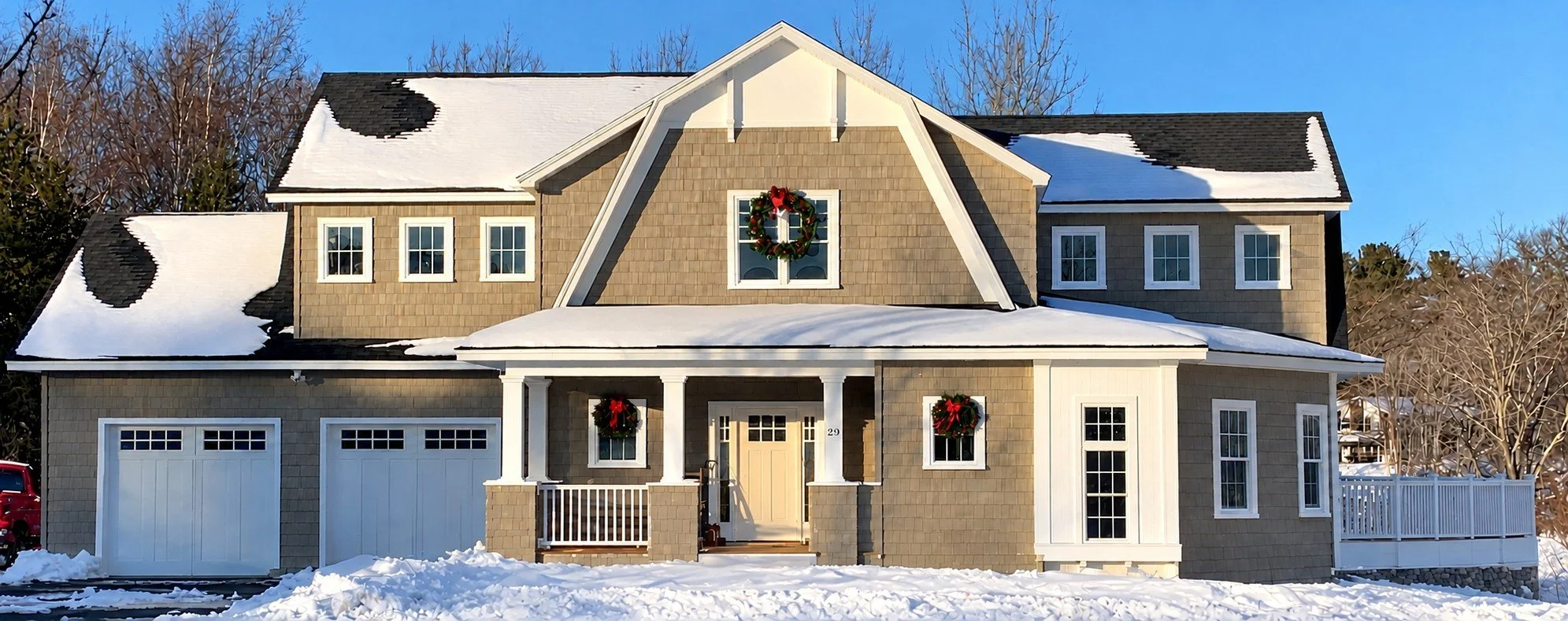 Gray shingle-style home with a covered front porch and two garage doors, with snow on the ground
