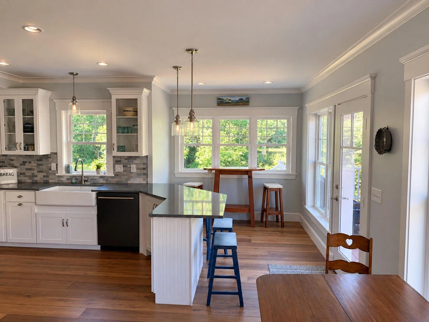 Kitchen and dining area with a white island, blue bar stools, and windows overlooking the yard