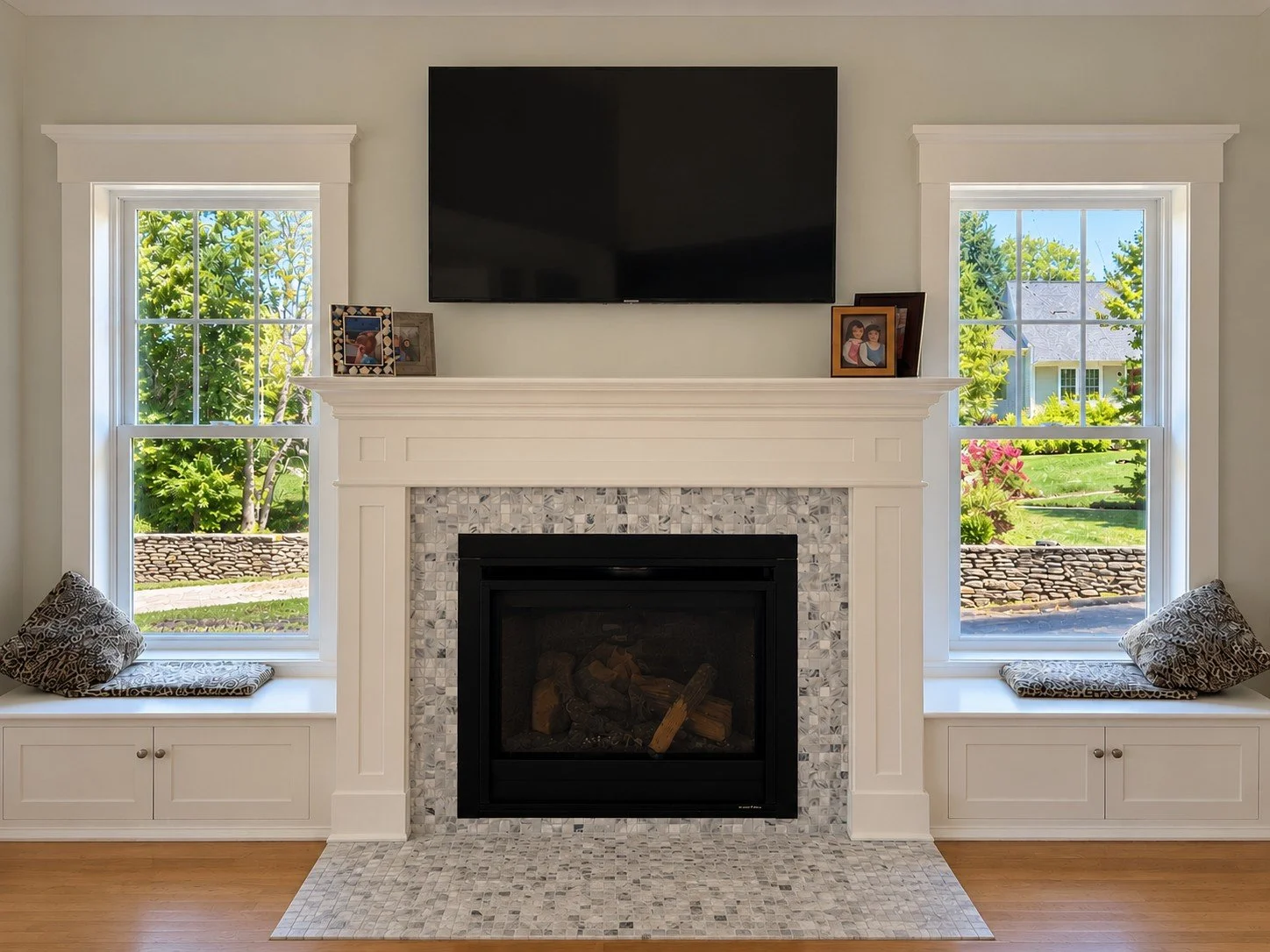 Fireplace with a mosaic tile surround and a wall-mounted TV between two windows with built-in window seats