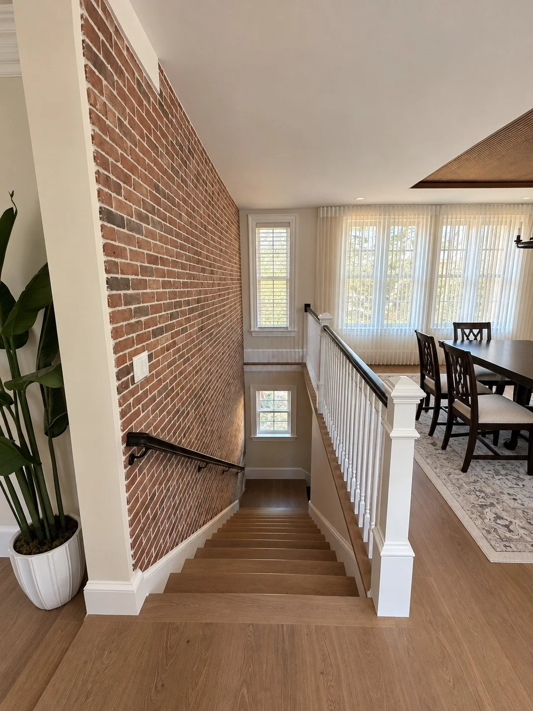 Stairway down beside an exposed brick wall with a white railing overlooking the dining room