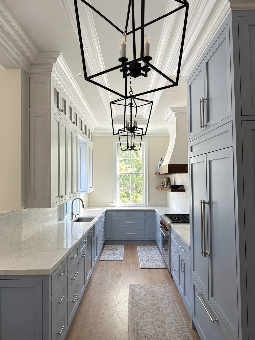 Galley kitchen with blue-gray cabinets, white quartz counters, black lantern pendants, and a paneled refrigerator