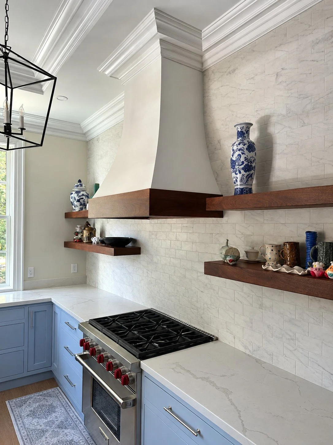 Kitchen range with a plaster hood, walnut floating shelves, and marble tile backsplash